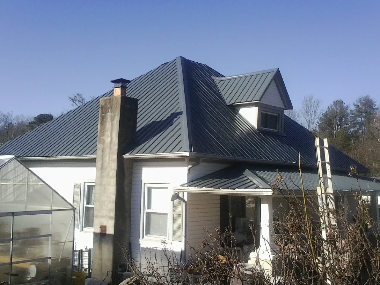 Dark blue standing seam metal roof on a white farmhouse with dormer in Westport Point