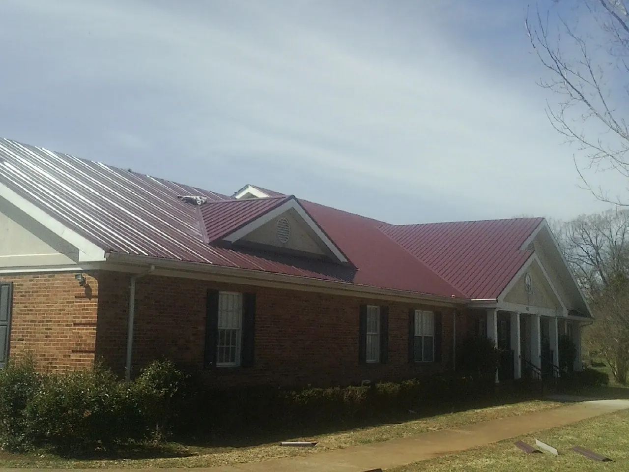 Red metal roof with gabled entries on a long brick building, from a Hail Damage Roof Repair job in Westport Point