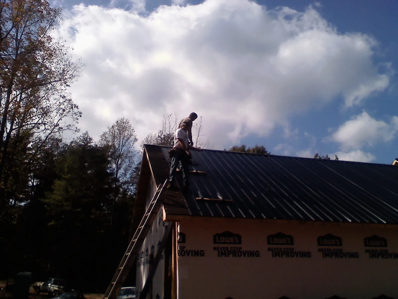 Roofer fastening dark metal panels high against a cloudy sky, from a Roof Inspection job in Westport Point