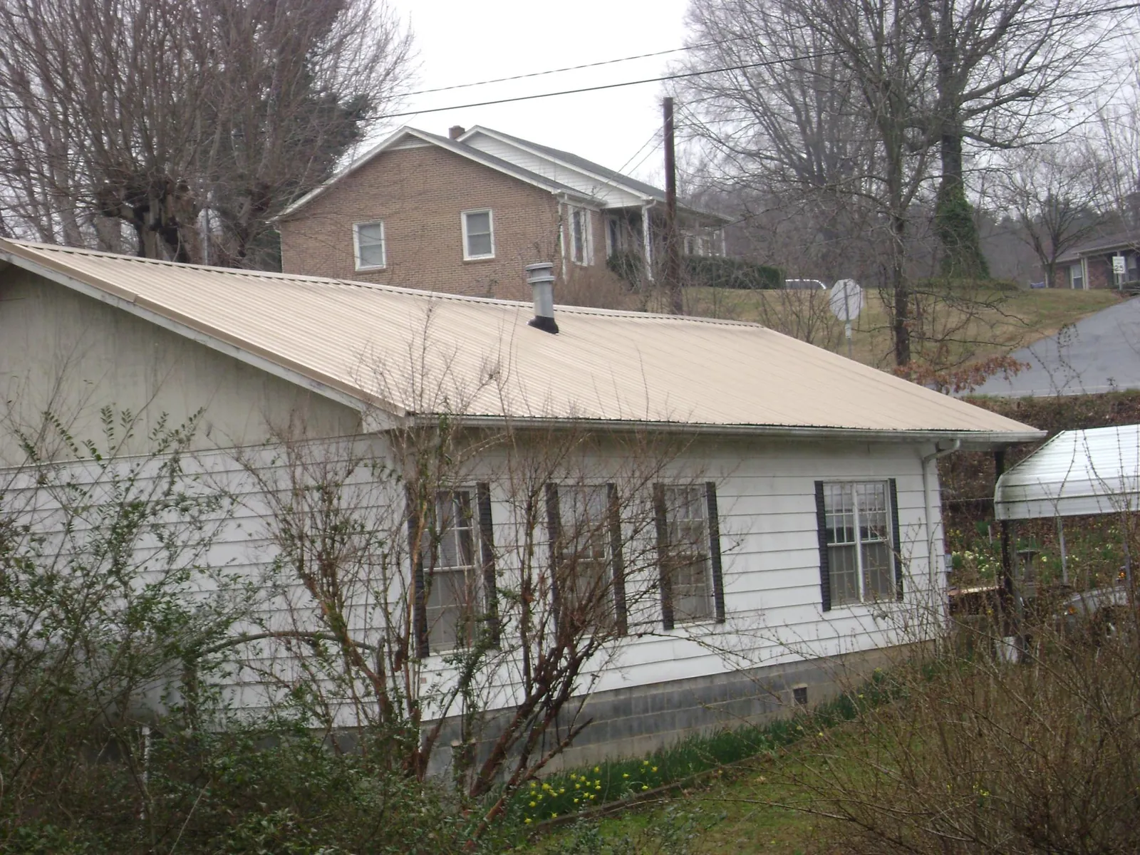 Tan metal roof on a white sided house set into a hillside — Commercial Roofing by Roofing Brothers in Westport Point