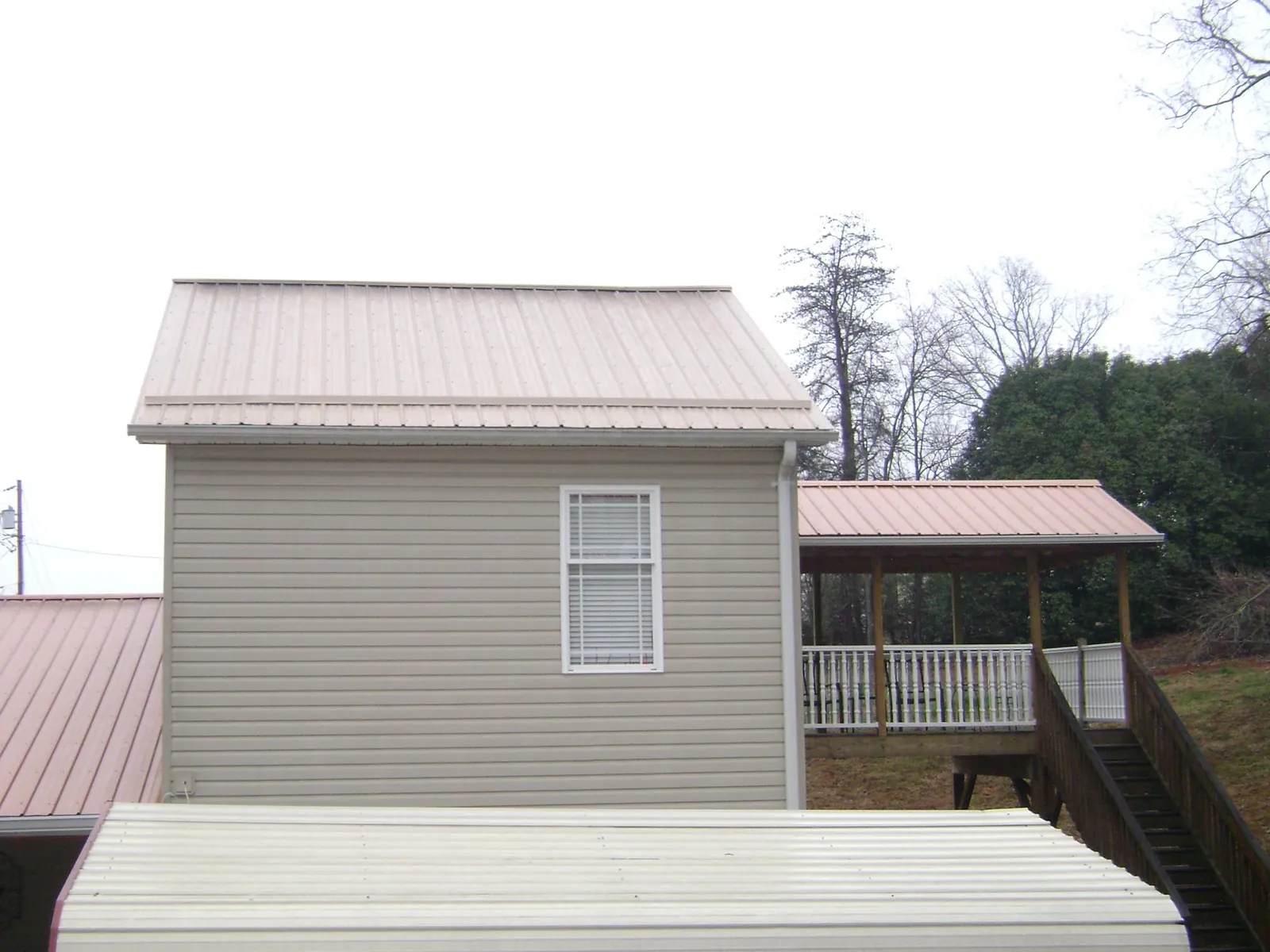 Tan metal roofs on a two story addition and attached porch, from a Roof Replacement job in Westport Point